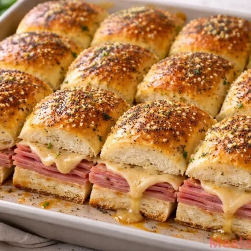 A tray of golden brown ham and cheese sliders on brioche rolls topped with poppy seeds