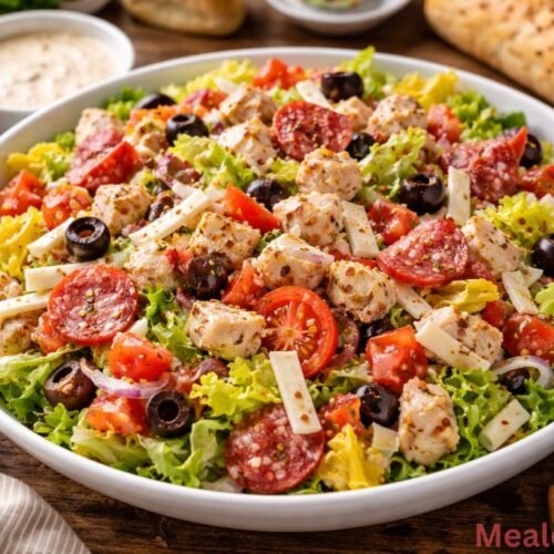 A large glass bowl filled with Italian Grinder Chicken Salad featuring shredded chicken, diced salami, pepperoni, and bright banana peppers
