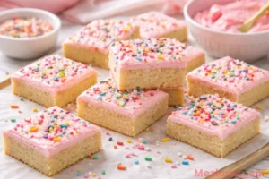 overhead shot of thick sugar cookie bars topped with pink buttercream frosting and colorful sprinkles
