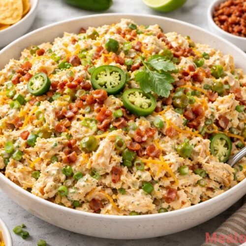 A large white bowl of creamy jalapeño popper chicken salad topped with bacon bits