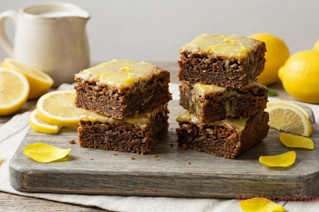 stack of glazed lemon brownies served on a white plate with fresh lemon slices on the side