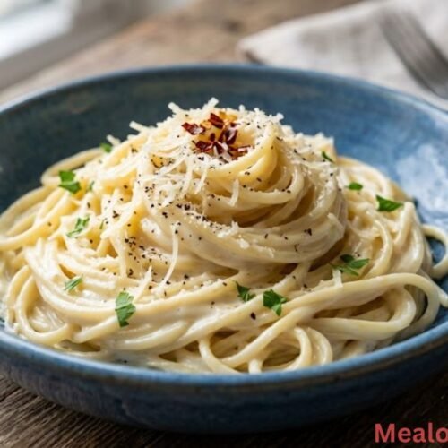 blue bowl filled with glossy cream cheese spaghetti garnished with freshly grated Parmesan and cracked black pepper