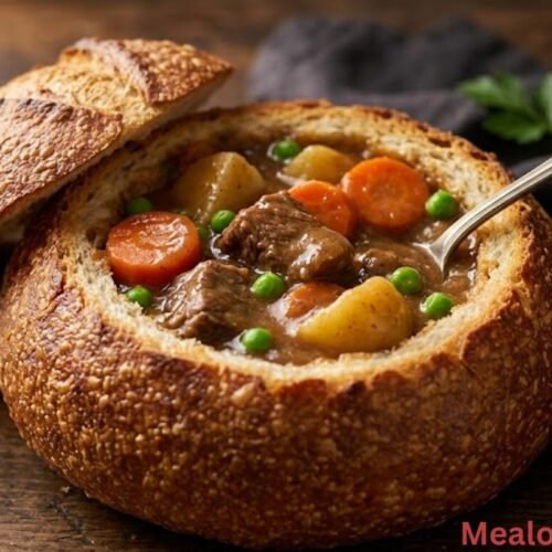 A steaming crusty bread bowl filled to the brim with thick, savory beef stew, carrots, and potatoes on a rustic wooden table